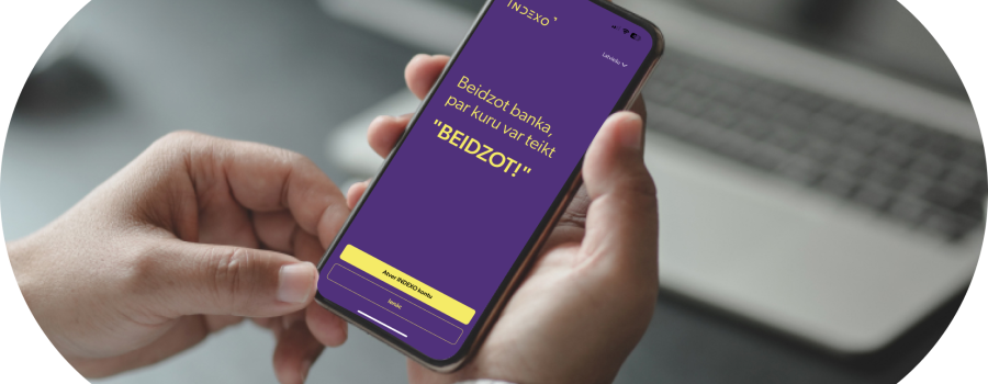 mobilo aplikāciju izstrādes paraugs indexo bankas aplikācija, kura redzama uz telefona, kuru tur rokās cilvēks.